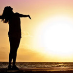 Woman with arms out at beach at sunset